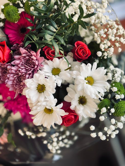 A vibrant floral arrangement featuring white daisies with bright yellow centers, deep pink roses, purple chrysanthemums with layered petals, and sprigs of delicate white baby's breath. The bouquet is 