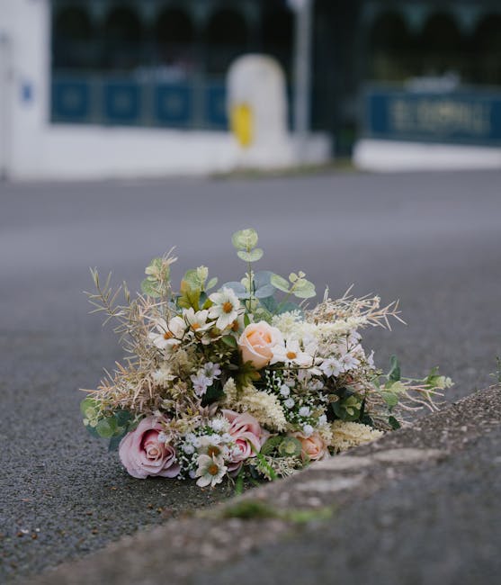 A delicate bouquet of fresh flowers resting on an outdoor pavement, featuring soft pink roses, white daisies, and small white filler flowers arranged with light green eucalyptus and wispy greenery. Th