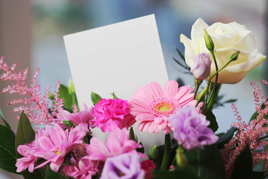 A vibrant floral arrangement featuring a mix of fresh, pink gerbera daisies, white roses, and pink carnations, accented with delicate pink astilbe and lush green foliage. The bouquet is wrapped in cle
