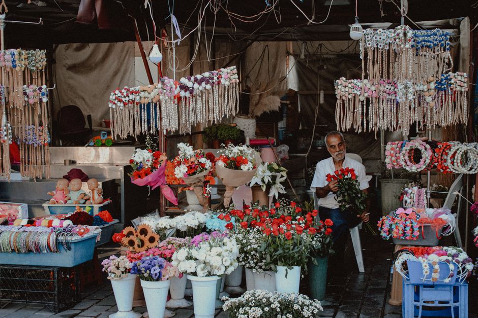 A flower stall featuring an array of fresh floral arrangements and bouquets, including red, white, pink, and purple flowers such as roses, daisies, and baby's breath, displayed in white and brown pots