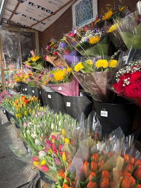 A vibrant display of freshly arranged flower bouquets at a florist stall, featuring a variety of colorful blooms including yellow chrysanthemums, pink tulips, orange tulips, red roses, purple irises,